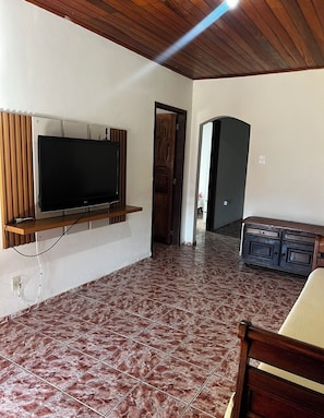 A room with a flat-screen TV mounted on the wall, a wooden bench, and a tiled floor.