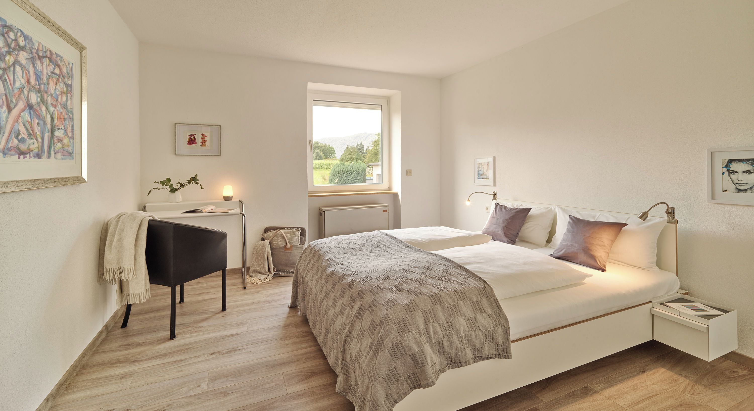 A bedroom with a bed, bedside tables, a desk, and a window.