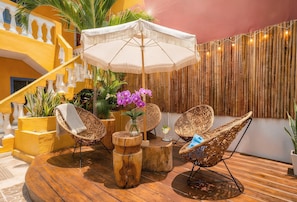 A tropical outdoor seating area with wicker chairs, a round wooden table, and a white umbrella. - Memory Foam King Bed - Easy Mornings. 5th Ave, ADO, Cozumel Ferry & Beach 4 Mins (Playa del Carmen)