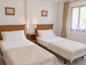 A hotel room with two single beds, a nightstand with a lamp, and a window with curtains. - Pueblo del Parque Pool View
Apartment | South-Facing Terrace | Walk to Beach (Benalmádena)