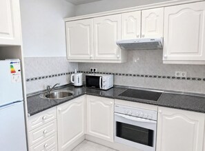 A kitchen with white cabinets, a microwave, a sink, and a stove. - Pueblo del Parque Pool View
Apartment | South-Facing Terrace | Walk to Beach (Benalmádena)