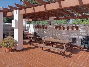 An outdoor patio area with wooden tables and chairs, potted plants, and a pergola structure. - Pueblo del Parque Pool View
Apartment | South-Facing Terrace | Walk to Beach (Benalmádena)