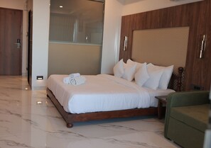 A hotel room with a large bed, a wooden headboard, a green armchair, and a marble floor.