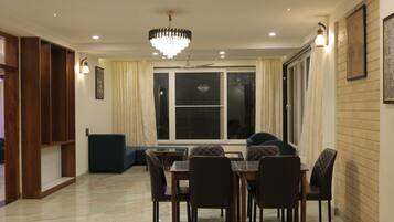Un comedor con candelabro, una mesa de comedor con sillas, un sofá y un ventanal con cortinas.