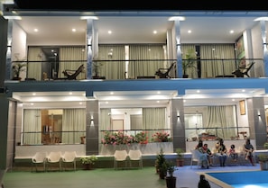 A hotel lobby with a seating area, a pool, and a balcony with chairs.