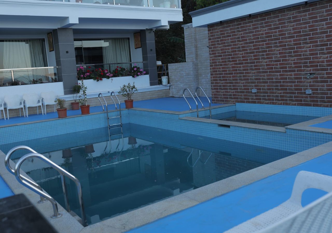 A swimming pool with steps and railings, surrounded by potted plants and a building with a balcony.