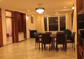 A dining area with a chandelier, a dining table with chairs, and a view of the outside through a large window.
