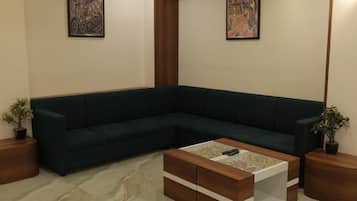 Una sala de estar moderna con un sofá seccional verde oscuro, una mesa de centro de madera con un objeto colorido encima y dos obras de arte enmarcadas en las paredes.