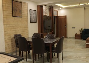 A dining area with a table and chairs, a television mounted on a wooden cabinet, and a brick wall with framed artwork. - Nivanta Grand Lake & Valley View Resort (Wai)