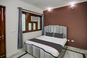 Un dormitorio con cama, ventana con cortinas, unidad de aire acondicionado y lámpara en la pared.