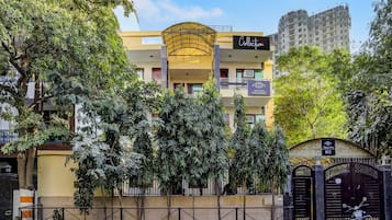 Um edifício de vários andares com fachada de vidro curva marcante, entrada fechada por portão e placas indicando um hotel chamado 'Tipsy Inn 2012'.