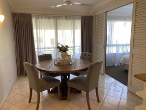 A dining area with a round table, six chairs, a vase with flowers, and a ceiling fan. - Cosy 1 Bedroom Unit centrally located in Cairns. (Cairns North)