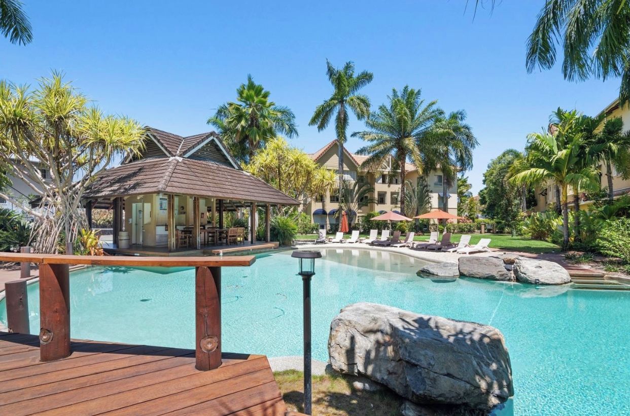 A resort with a swimming pool, lounge chairs, and palm trees.