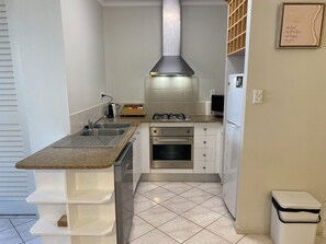 A compact kitchen with a gas stove, oven, and a built-in range hood. - Cosy 1 Bedroom Unit centrally located in Cairns. (Cairns North)