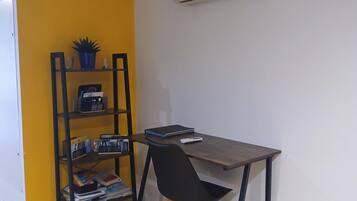 Una habitación con un escritorio, una silla y una estantería frente a una pared amarilla.
