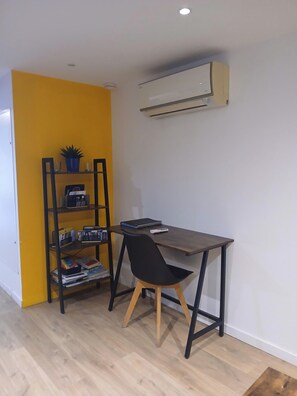 Ein Zimmer mit Schreibtisch, Stuhl und einer Bücherwand an einer gelben Wand.