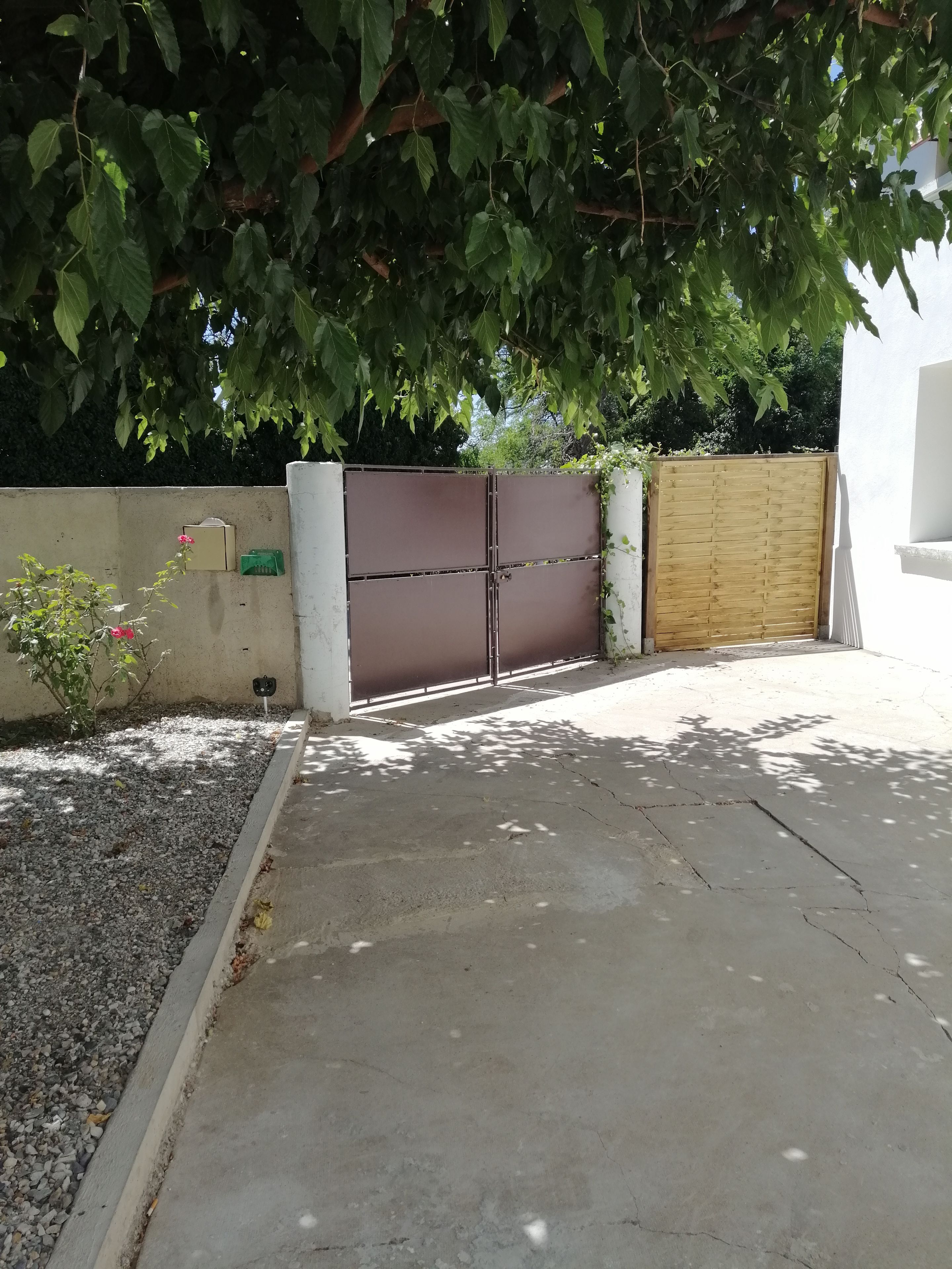 Una entrada cerrada con un camino de hormigón, una verja de metal y una cerca de madera.