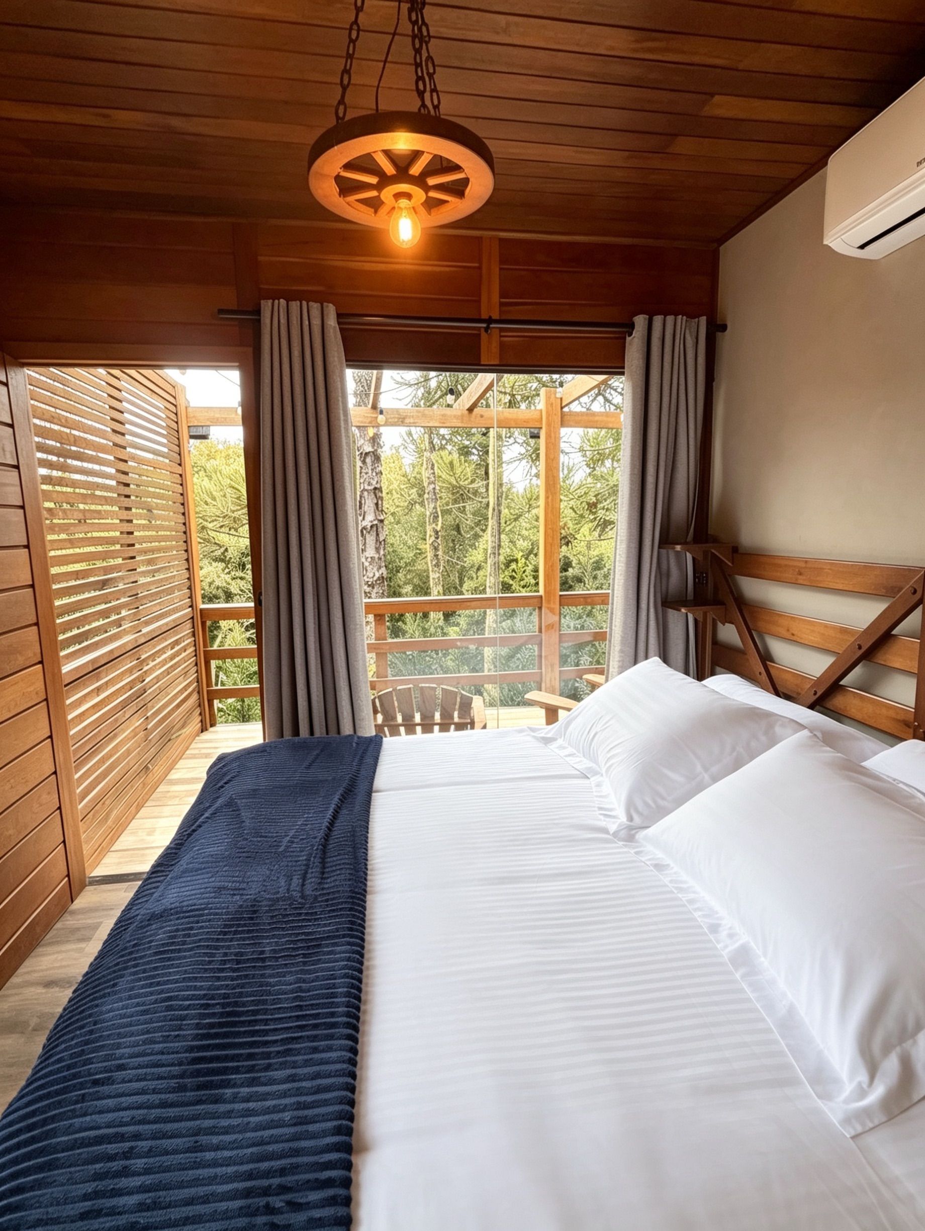 Ein Schlafzimmer mit einem Bett, einer Hängelampe, einem Fenster mit Vorhängen und Blick auf Bäume.