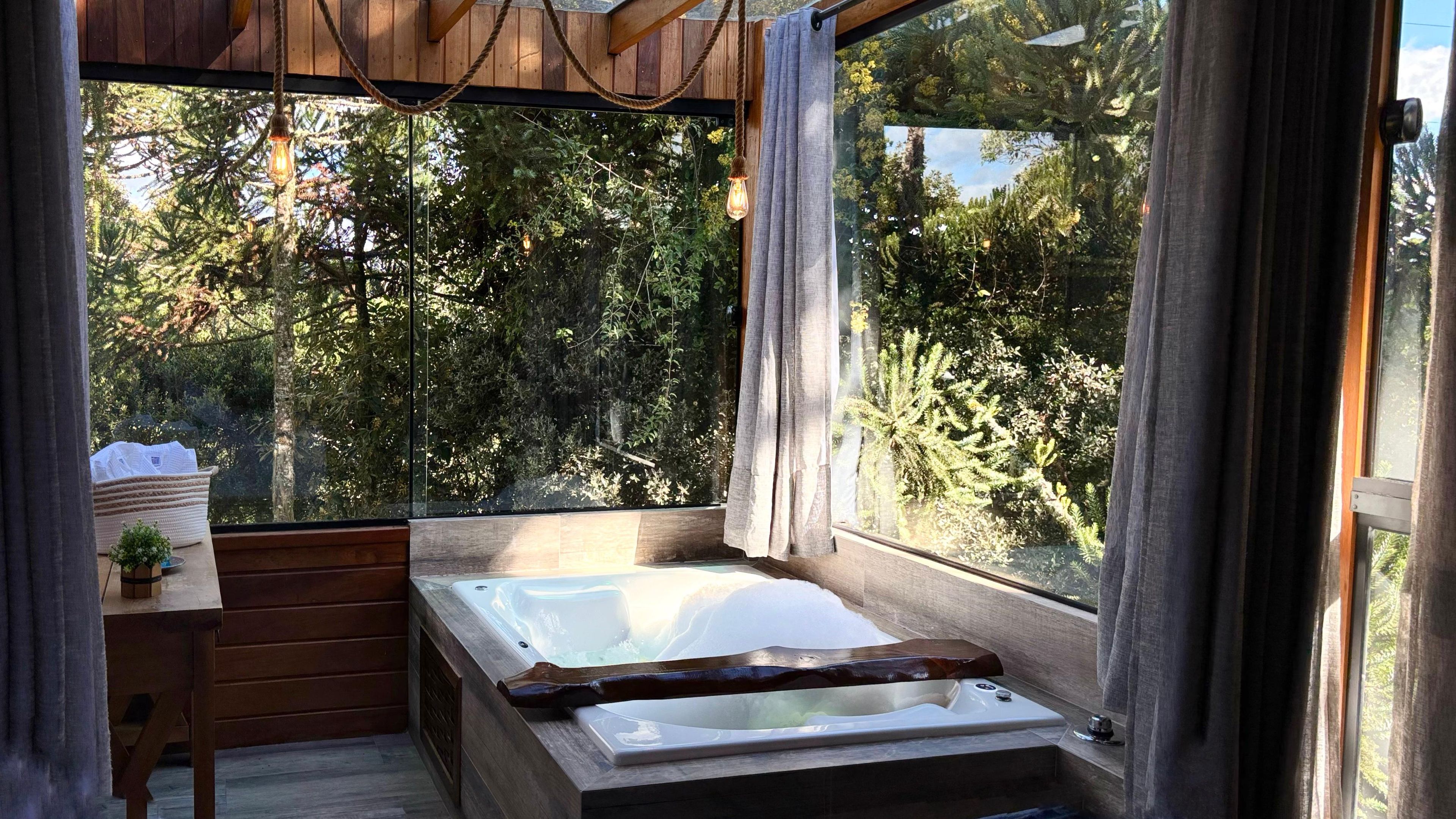 A wooden cabin with a large window, a wooden bench, a small table with a plant, and a hot tub.