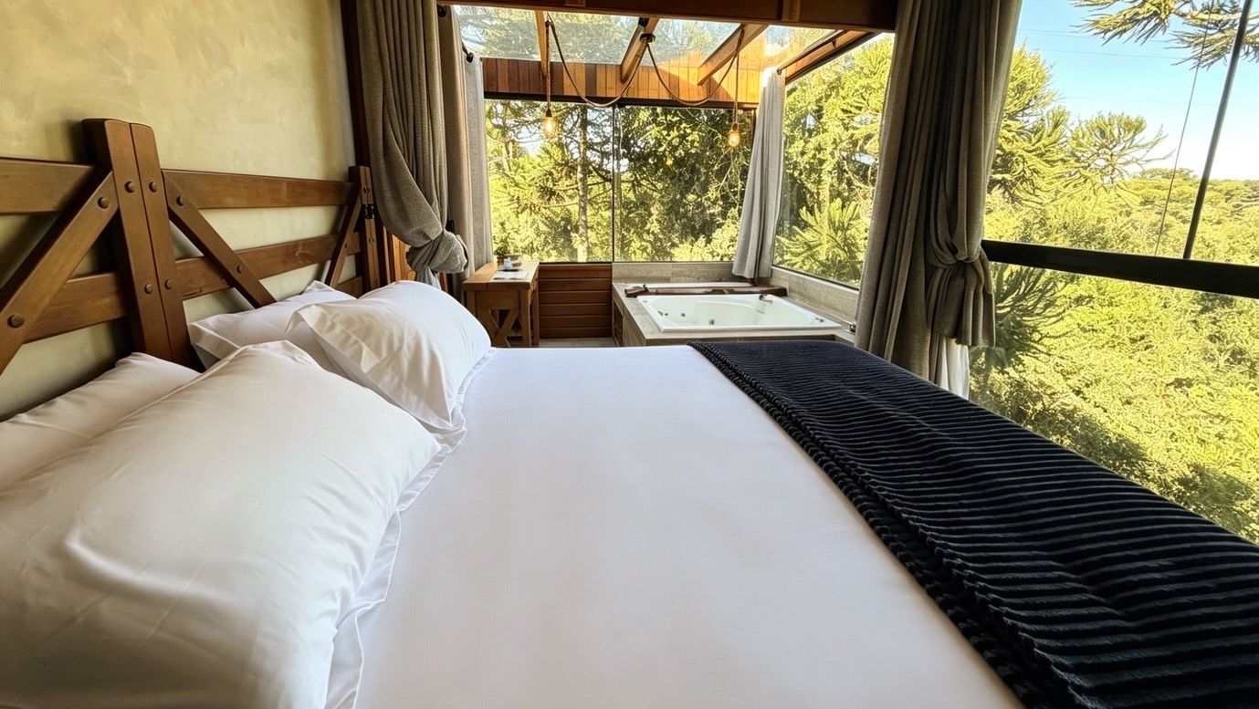 Un lit avec du linge de lit blanc, une tête de lit en bois et une vue sur un paysage naturel par la fenêtre.