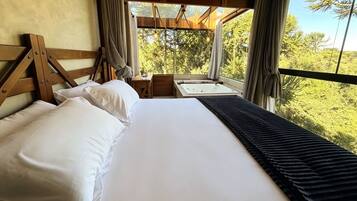 Un lit avec du linge de lit blanc, une tête de lit en bois et une vue sur un paysage naturel par la fenêtre.