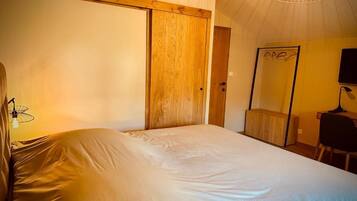 Un dormitorio con una cama, una puerta de madera, un espejo y un escritorio con una silla.