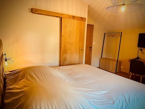 A bedroom with a bed, a wooden door, a mirror, and a desk with a chair. - Prim'tout (Ohey)