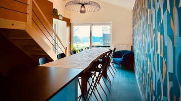 Una cocina moderna con una larga mesa de comedor, una escalera de madera y arte abstracto en la pared.