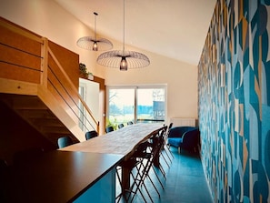 A modern kitchen with a long dining table, wooden staircase, and abstract wall art. - Prim'tout (Ohey)