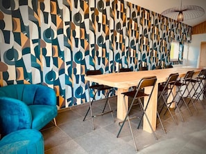 Un espace repas moderne avec une longue table en bois, des chaises pliantes et un motif mural abstrait et dynamique.
