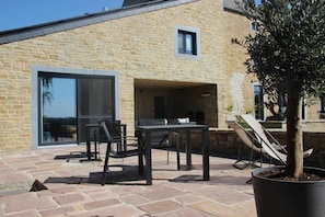 Un bâtiment en pierre doté d’un patio comprenant une table et des chaises, un arbre en pot et un petit espace de détente extérieur.