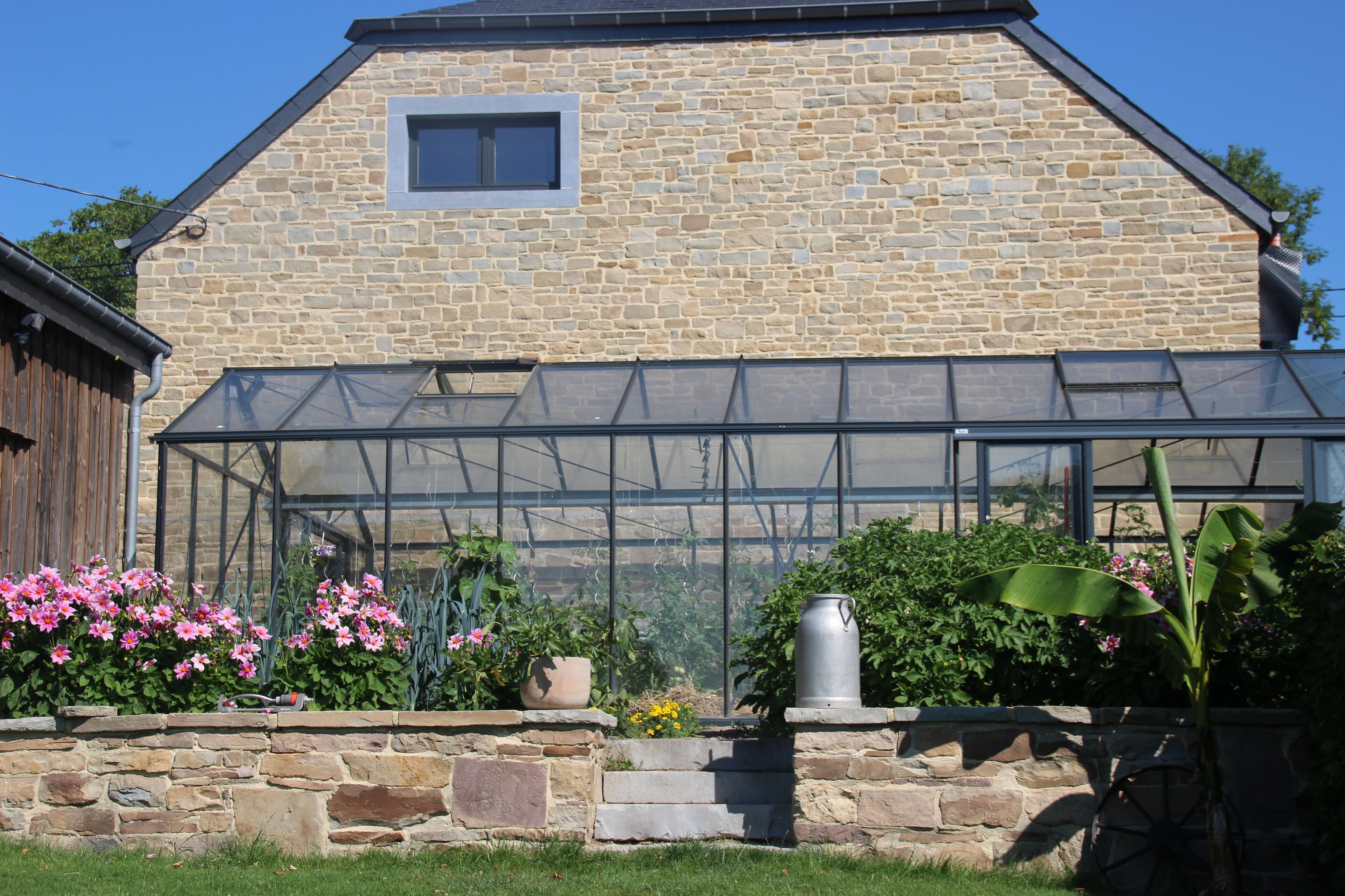 Une maison en pierre avec une grande serre en verre.