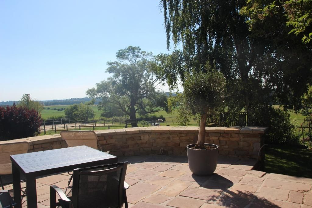An outdoor patio with a table and chairs, a potted tree, and a stone wall.
