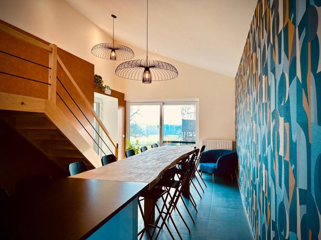 A modern kitchen with a long dining table, wooden staircase, and abstract wall art.
