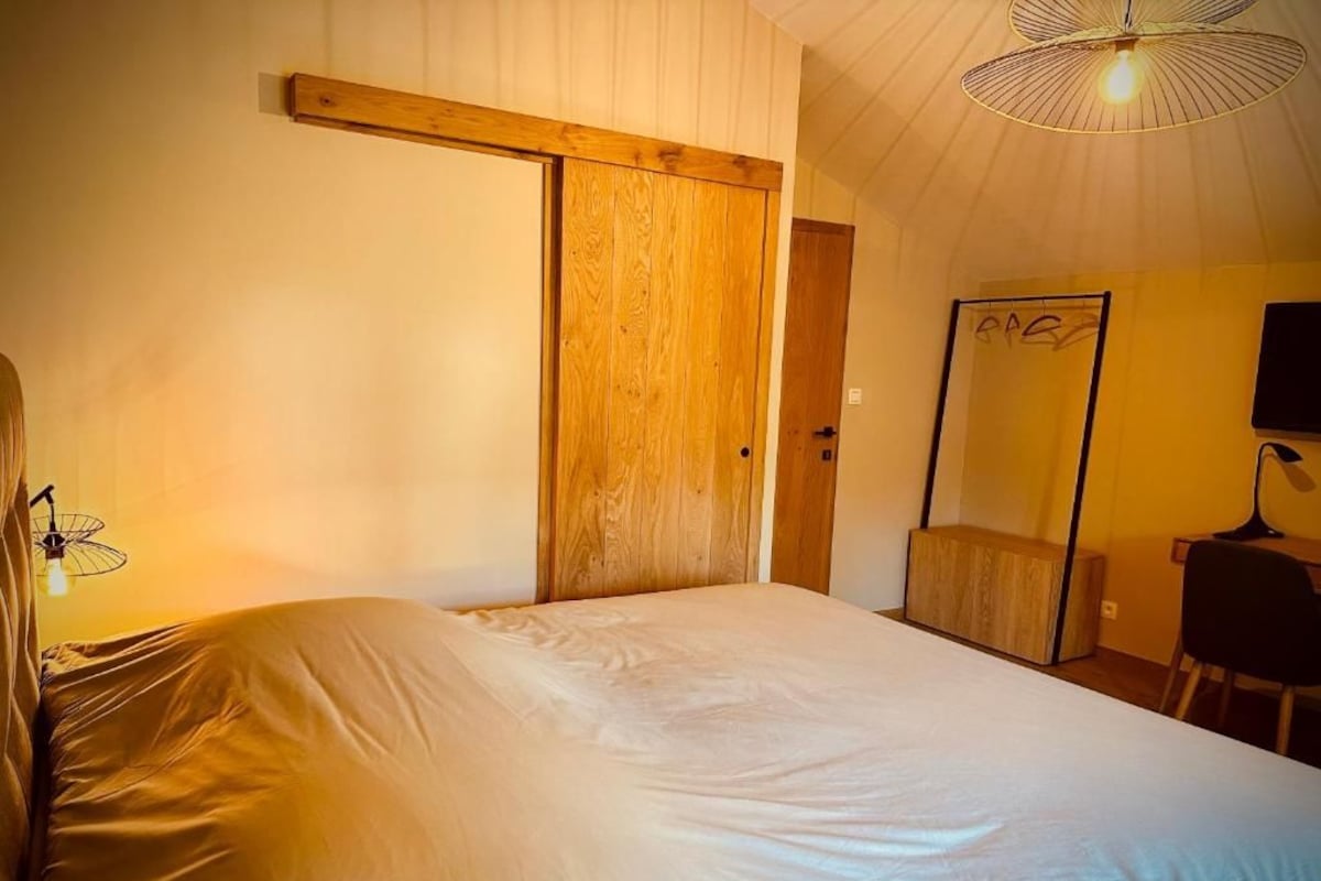 A bedroom with a bed, a wooden door, a mirror, and a desk with a chair.