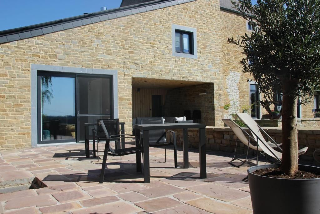 A stone building with a patio area featuring a table and chairs, a potted tree, and a small outdoor seating area.