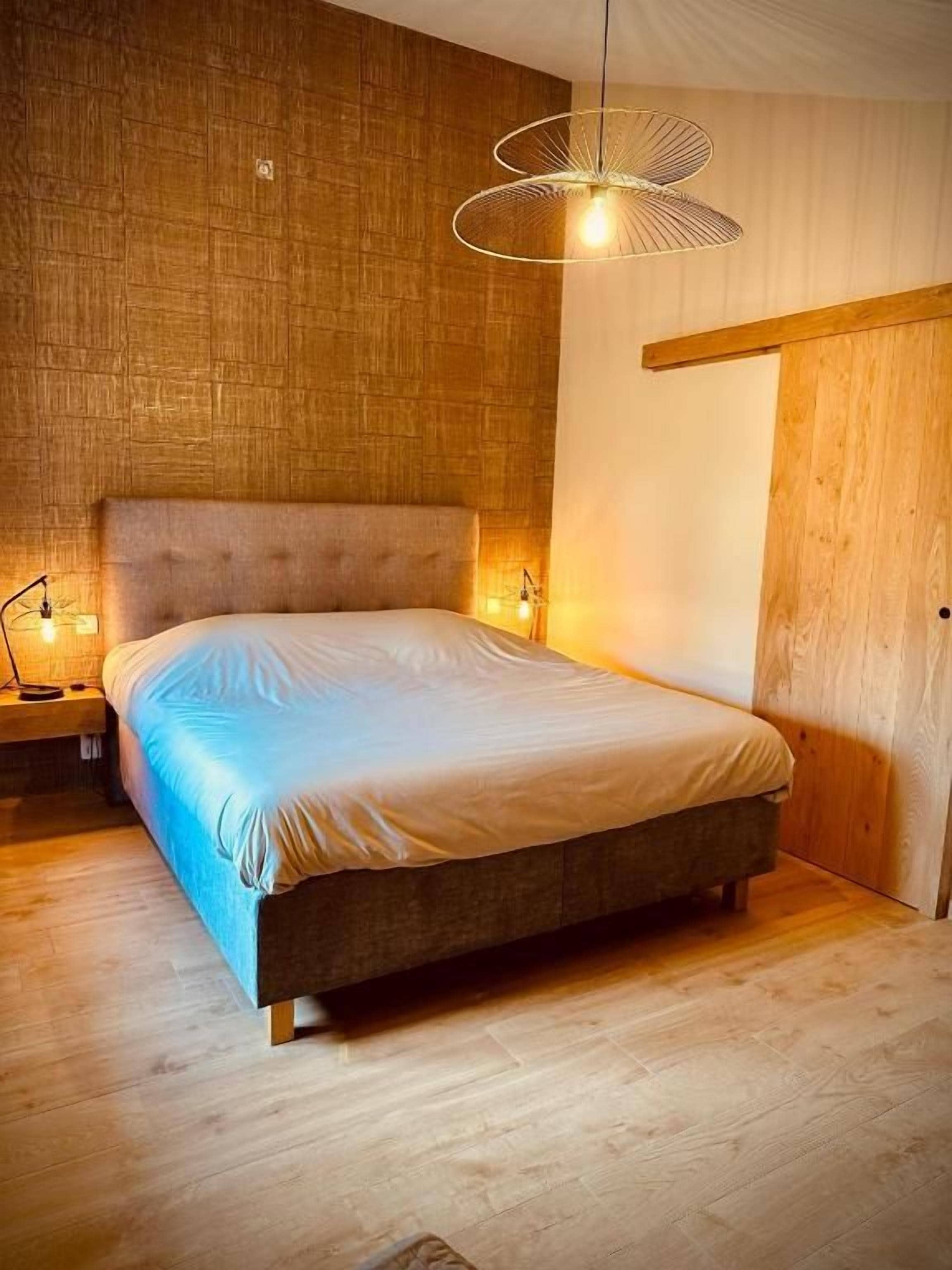 Ein Schlafzimmer mit einem Holzkopfteil, einem Bett mit einer weißen Matratze und einer hängenden Lampe.