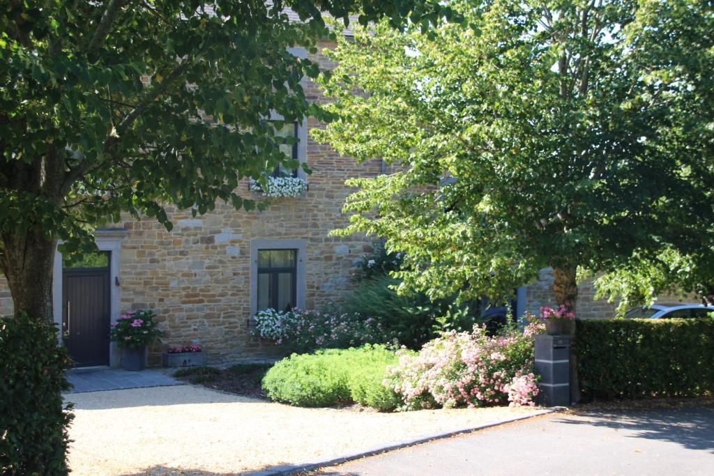 Un bâtiment en pierre avec une allée de gravier, entouré d’une végétation luxuriante et de plantes en fleurs.