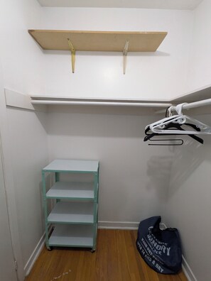 A small storage closet with a metal shelf, a metal cart, and a bag hanging on a hook. - Room #3 - Queen Size Bedroom in Shared Townhouse (Toronto)