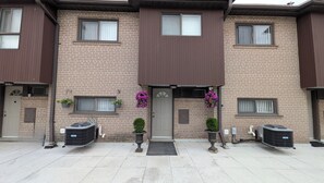 A residential building with a brown facade, numbered doors, and outdoor air conditioning units. - Room #3 - Queen Size Bedroom in Shared Townhouse (Toronto)