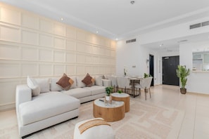 A modern living room with a sectional sofa, round coffee table, and dining area with chairs. - Premium 4BR at Sky View Tower (Dubai)
