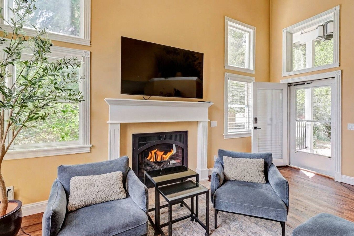 Una sala de estar con chimenea, dos sillones, una mesa de centro y un televisor de pantalla plana grande sobre la chimenea.