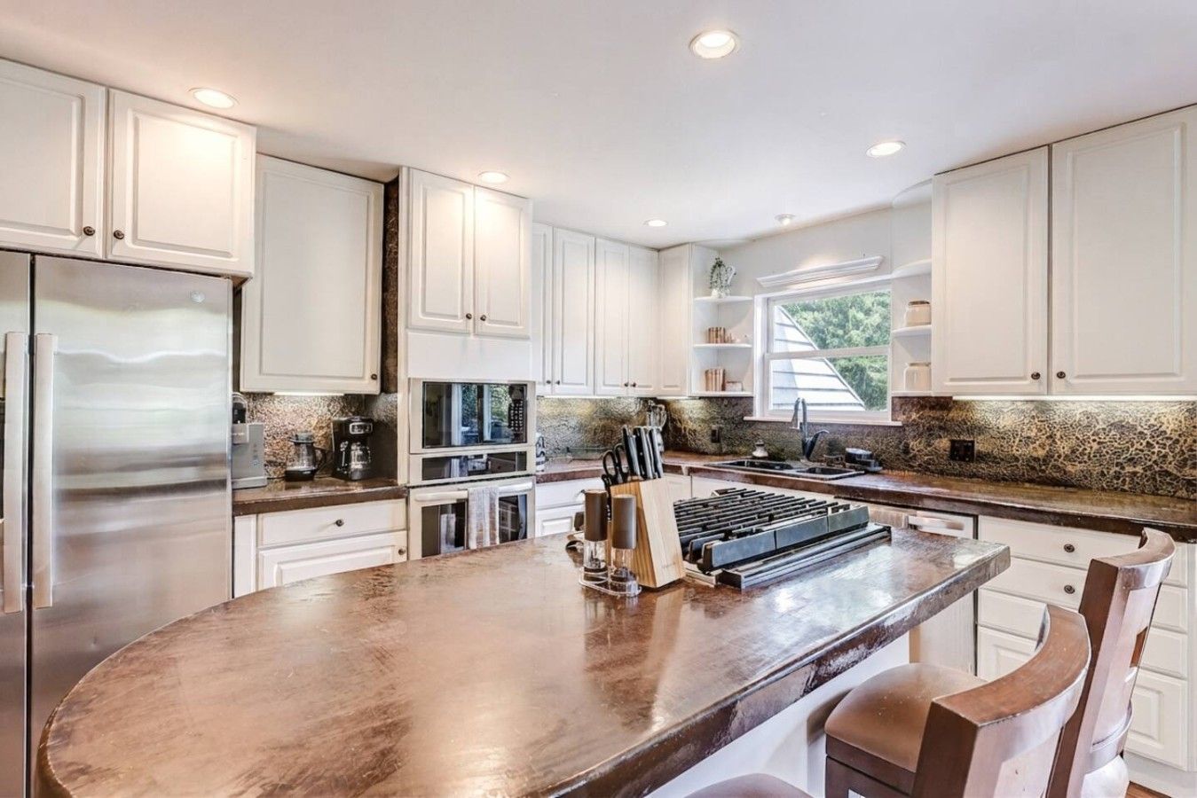 Una cocina moderna con armarios blancos, una isla central y un refrigerador de acero inoxidable.