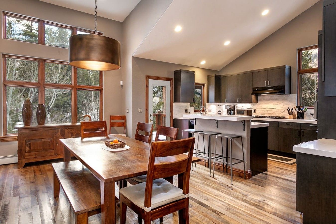 A modern kitchen with a central island, wooden dining table, and bar stools.
