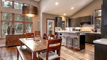 A modern kitchen with a central island, wooden dining table, and bar stools.