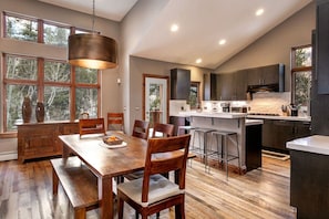 A modern kitchen with a central island, wooden dining table, and bar stools.
