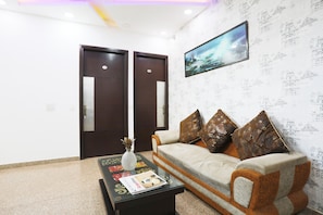 A room with a sofa, a coffee table with magazines, a decorative vase, and a framed picture on the wall. - Collection O Tipsyy Inn (Gurugram)