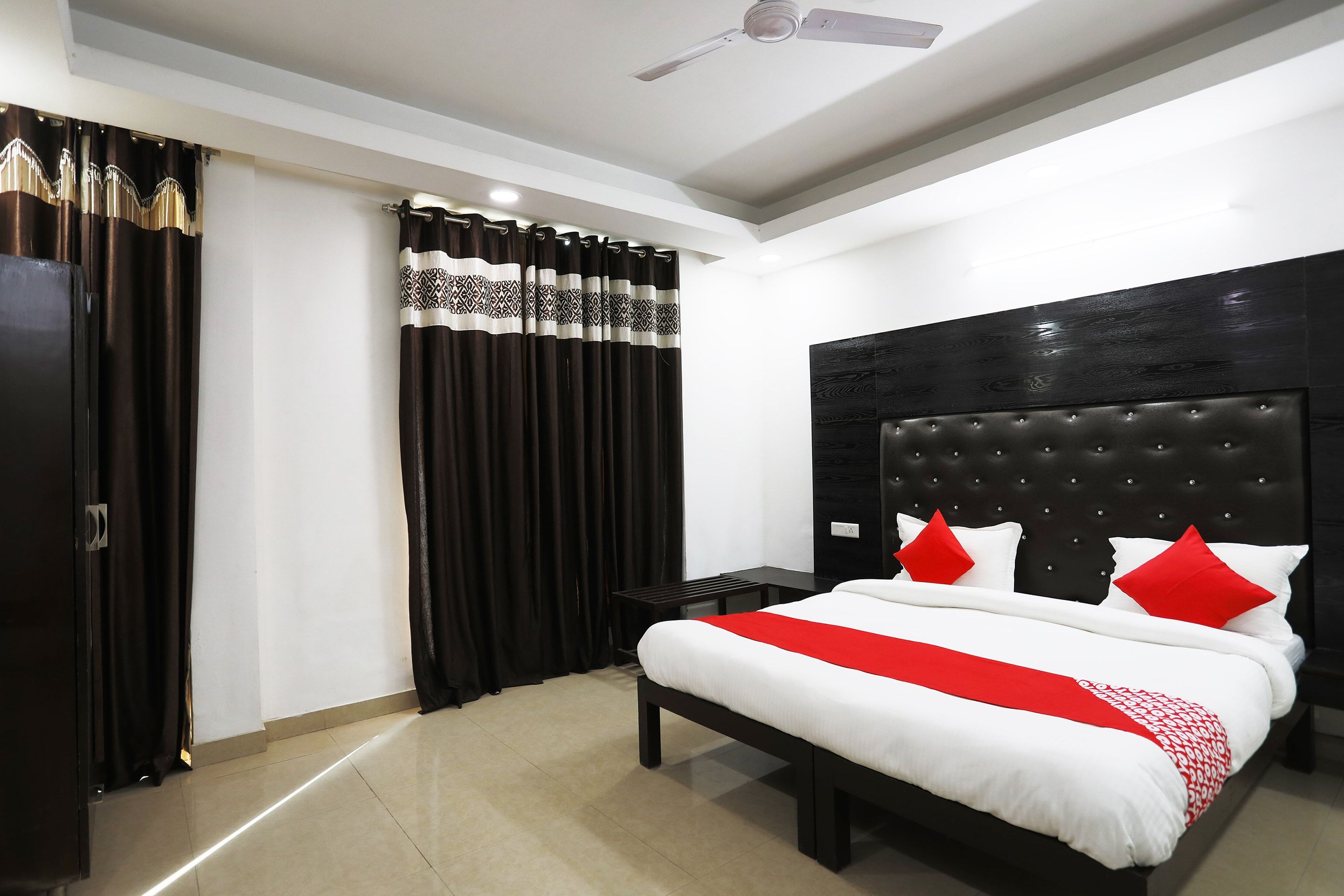 A hotel room with a bed, a nightstand, a ceiling fan, and a window with curtains.