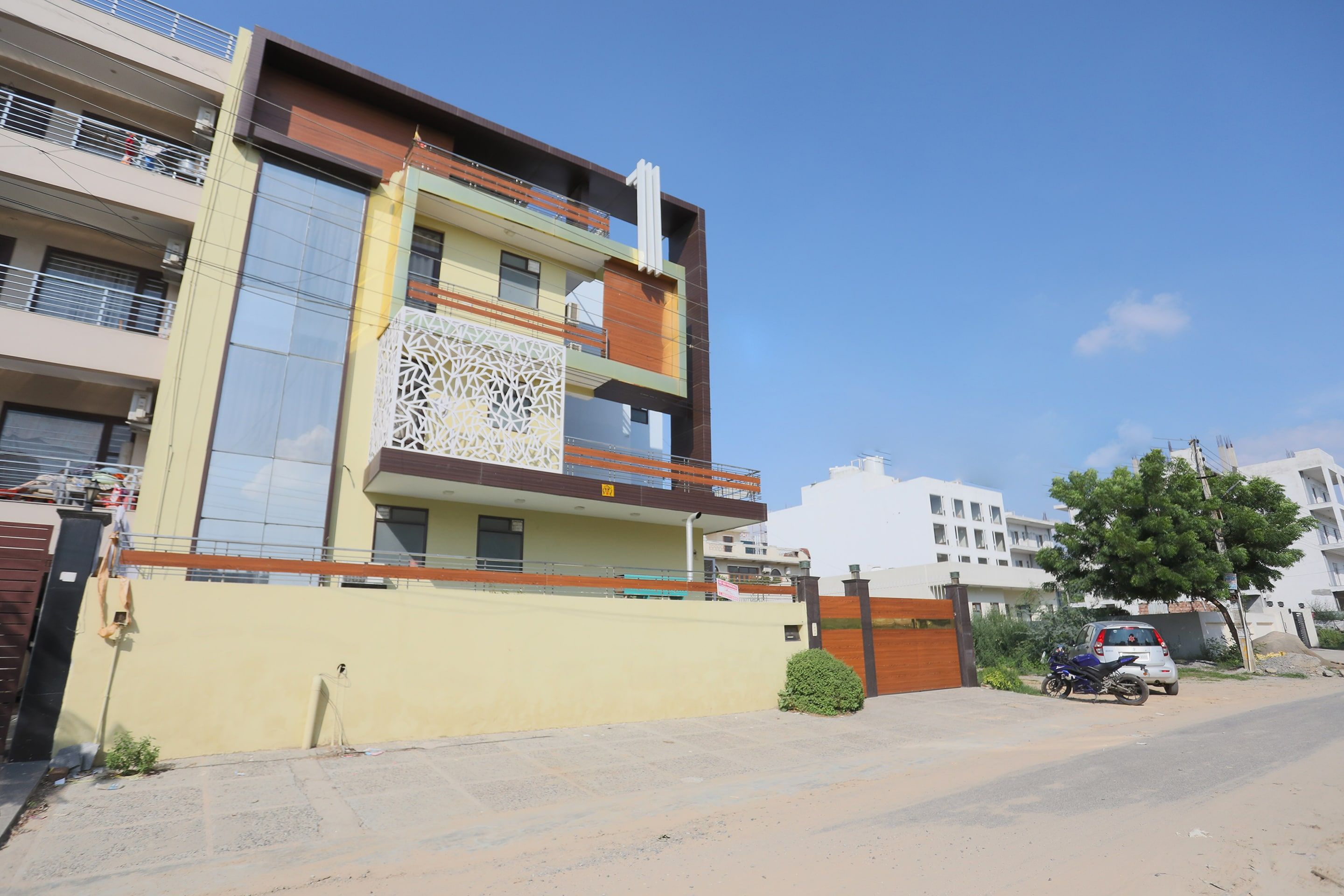 A multi-story residential building with balconies, a gated entrance, and a parked motorcycle.