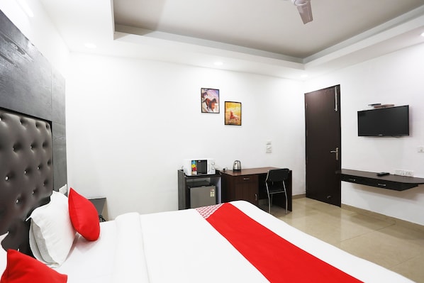 A hotel room with a bed, a desk, a chair, a television, and a door. - Collection O Tipsyy Inn (Gurugram)